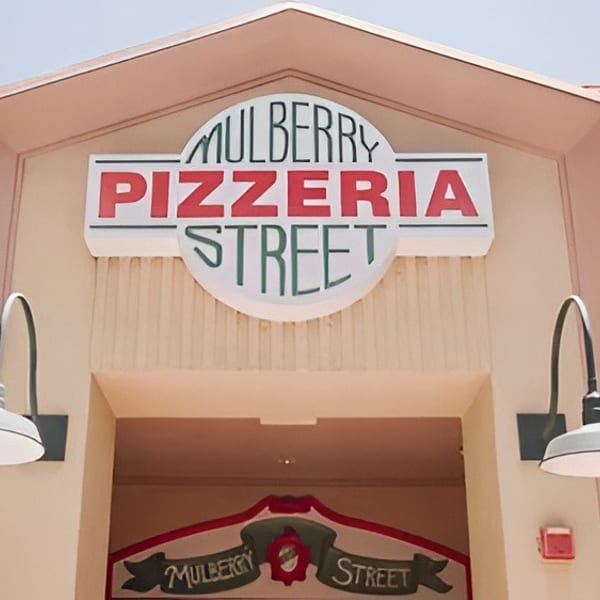 Mulberry Pizzeria Street sign on a light-colored building with two outdoor lamps and a red roof.