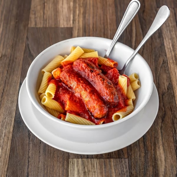 Rigatoni pasta with two sausages in red marinara sauce, served in a white bowl with forks.