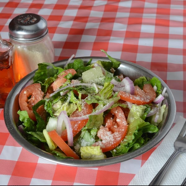 Fresh garden salad with lettuce, tomatoes, onions, and cheese on a red and white checkered tablecloth.