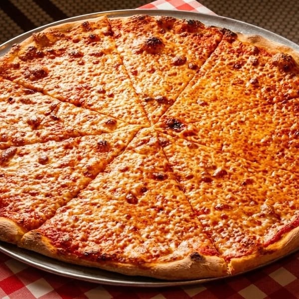 A large, sliced cheese pizza on a metal tray, resting on a red and white checkered tablecloth.