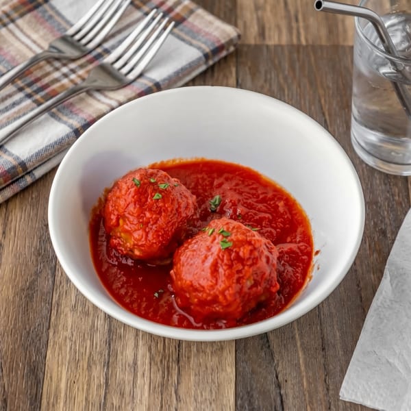 Two large meatballs in red sauce, garnished with parsley, in a white bowl on a wooden table.