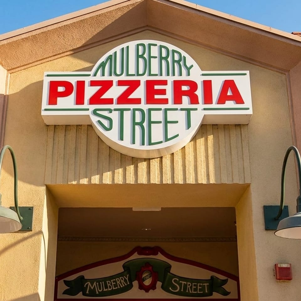 Mulberry Pizzeria Street sign with red and green letters on a beige building facade.