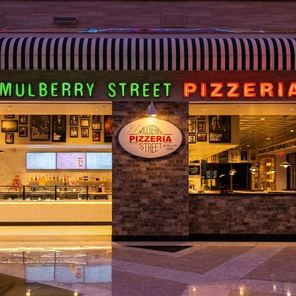 Mulberry Street Pizzeria storefront with neon signs, a striped awning, and a bright, inviting interior.